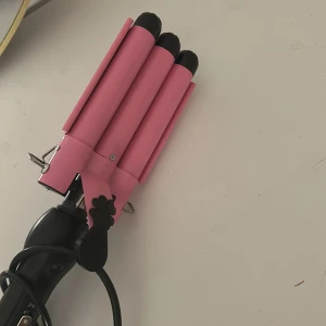 3-Barrel Curling Iron Pink - Snygg rosa locktång med tre värmeelement för vågigt hår. Justerbar temperatur mellan 180°C och 210°C. EU-kontakt. Ser ut att vara i gott skick utan synligt slitage. Perfekt för att skapa stora, mjuka vågor snabbt och enkelt.