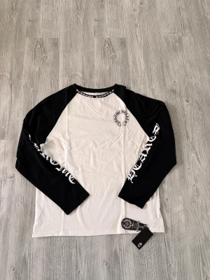 Chrome Hearts svartvit långärmad tröja - Säljer en svartvit långärmad tröja från Chrome Hearts med kontrastfärgade ärmar och stort tryck på ryggen. Tröjan har coolt tryck längs ärmarna och runt halsen, samt klassisk logga på bröstet. Tillverkad i mjuk bomull. Pris kan diskuteras vid snabb affär. :)