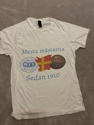 Vit MFF t-shirt med tryck - Hej! Säljer en vit t-shirt från Malmö FF med stort tryck på framsidan. Tröjan är i bra skick och egendesignad, kostade ca 400 kr att göra.