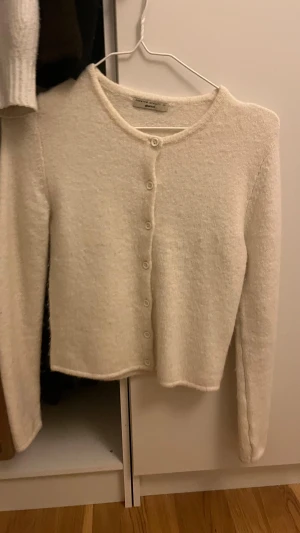 Beige stickad kofta från Gina Tricot - Mysig beige stickad kofta från Gina Tricot i storlek XS. Koftan har rund hals, långa ärmar och knäppning med små matchande knappar framtill. Perfekt för lager-på-lager och har en mjuk, fluffig känsla som gör den extra skön.