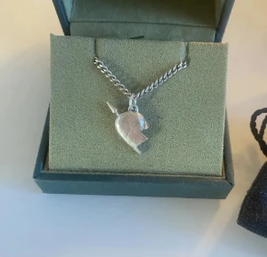 Maria Nilsdotter Halsband - Unikt halsband i silver med en berlock formad som en hjälm, hängande på en grov kedja. Perfekt för dig som gillar detaljer med lite edge och vill sticka ut med ett coolt smycke. Kommer i en snygg ask.