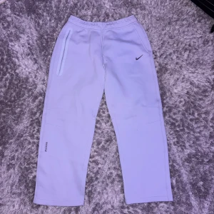Helt Nya Baby Blue Nike NOCTA  mjukisbyxor M - Nike NOCTA mjukisbyxor i ljuslila (ser mer ut som baby blue men egentligen heter ljuslila) med elastisk midja och snörning. Snyggt Swoosh på framsidan och NOCTA-logga på benet. Byxorna har raka ben och praktiska fickor med dragkedja. Perfekt för chill eller streetwear. HELT NYA! ALDRIG ANVÄNDA