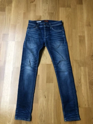 Slim fit jeans från Jack & Jones - Snygga blå slim fit jeans från Jack & Jones, modell Tim. Klassisk femficksdesign med normal midja och raka ben. Jeansen har en cool tvätt med lätt slitningar och är tillverkade i mjukt denim-material som sitter skönt hela dagen.