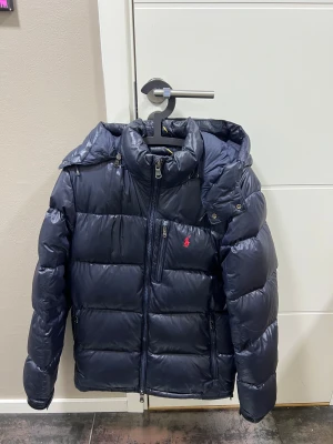 Marinblå pufferjacka från Polo Ralph Lauren - Säljer denna trendiga pufferjacka från Polo Ralph, då jag är sugen på något nytt! Jackan är i fint skick och väl omhändertagen. Inköptes november 2023 från Zalando! 