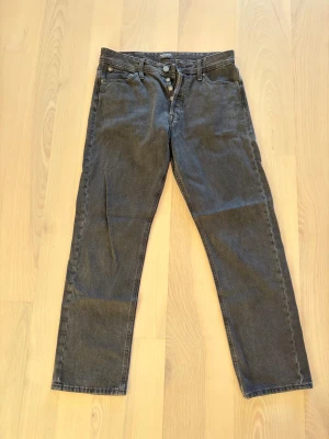 Svarta relaxed jeans Jack & Jones 31/32 - Svarta jeans från Jack & Jones, modell Relaxed/Chris. Klassisk femficksdesign med raka ben och knappgylf. Jeansen har en avslappnad passform och är tillverkade i slitstarkt bomullsmaterial. Perfekt för dig som gillar en chill och enkel stil.