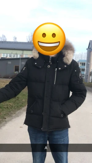 Svart dunjacka med päls från Moose Knuckles - Svart dunjacka från Moose Knuckles med fluffig beige päls på huvan, silverfärgade dragkedjor och coola detaljer på ärmen. Jackan har flera fickor med knappar och dragkedjor, samt en snygg logga på armen. Perfekt för kalla vinterdagar.