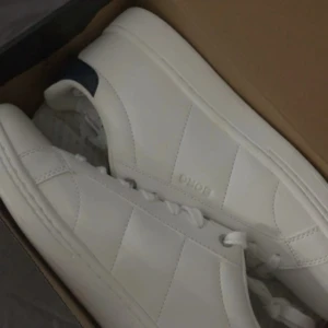 Vita sneakers från Björn Borg - Fräscha vita sneakers från Björn Borg med stilren design och diskret logga på sidan. Skorna har rund tå, platt sula och klassisk snörning. Materialet är slätt skinn och hälen har en mörkblå detalj som ger extra edge. Perfekta för dig som gillar minimalistisk stil.