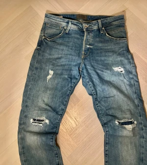 Slim fit blå jeans Jack & Jones - Säljer ett par blå slim fit jeans från Jack & Jones, modell Glenn. Jeansen har superstretch, slitna detaljer och hål på benen för en cool look. Klassisk femficksmodell med dragkedjegylf och normal midja.