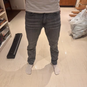 Grå jeans från Woodbird, storlek 29/34 - Säljer ett par grå jeans från Woodbird i storlek 29/34. Jeansen har raka ben och en snygg tvättad grå färg. Tillverkade i bomull med en cool, avslappnad look! Använda några gånger men inga tydliga defekter! Min kille är 187 cm lång! 