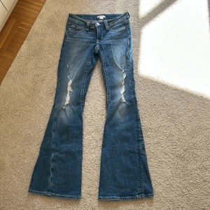 Blå bootcut jeans från Gina Tricot XS - Snygga blå bootcut jeans från Gina Tricot i storlek XS. Jeansen har slitna detaljer framtill, klassiska fickor och markerade sömmar. Baktill finns fickor med lock och knapp. Perfekta för dig som gillar retrovibbar och utsvängda ben.