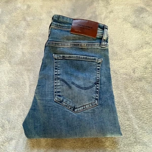 Blå jeans från Jack & Jones 30/32 - Snygga blå jeans från Jack & Jones med klassisk femficksdesign och läderpatch bak i midjan. Jeansen har en rak passform och är tillverkade i slitstarkt denimtyg. Perfekta för en avslappnad och trendig look.Storlek 30/32