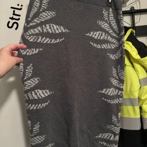 Grå långkjol med mönster från Apart storlek: 38 - Säljer en grå långkjol från Apart med stickat material och ljusgrått bladliknande mönster. Kjolen har en mjuk och stretchig midja och är perfekt för dig som gillar en chill och snygg look. Passar till många olika stilar och är superbekväm.