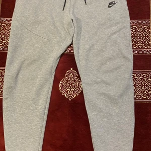 Grå mjukisbyxor från Nike M - Snygga grå mjukisbyxor från Nike i storlek M. Byxorna har dragsko i midjan, smal passform och diskret Nike-logga på låret. Perfekta för chill eller träning, tillverkade i mjukt bomullsmaterial för extra komfort.