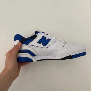 New Balance 550 vit/blå sneakers - Säljer ett par New Balance 550 sneakers i vitt och blått med svarta detaljer. Kvitto finns via mail, sko box finns! 📦 