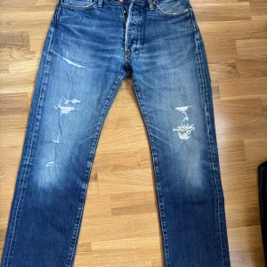 Acne jeans - Snygga blå jeans från Acne med slitna detaljer och raka ben. Klassisk femficksmodell med knappar framtill och tydliga slitningar på låren för en cool, avslappnad look. Tillverkade i robust denim med autentisk tvättad finish.