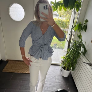 Randig omlottblus med knyt i midjan - Säljer en blåvit randig omlottblus med v-ringning och knyt i midjan. Blusen har trekvartsärmar och en snygg, figurnära passform. 