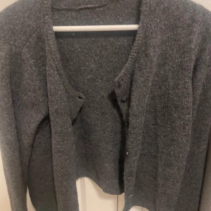 Mörkgrå kofta från 157 i ull - Mysig mörkgrå kofta från 157 i storlek L. Koftan är stickad i ull och har knappar framtill. Perfekt för lager-på-lager och passar till allt när det är kallt ute. Storleken är L men den har blivit mindre och liten i storlek så det är S/Xs