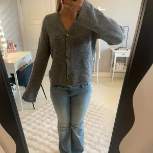 Grå kofta från 157 med knappar - Mysig grå kofta från 157 med v-ringning och tre stora knappar framtill. Koftan är stickad och har långärmad passform med lite loose fit. Perfekt att slänga på sig när det är kyligt ute.