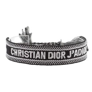 Christian Dior svart/vitt armband - Snyggt vävt armband från Christian Dior med texten 'J'ADIOR' i vitt på svart bakgrund. Armbandet har justerbar knytning med tofsar i ändarna och coola detaljer längs kanterna. Perfekt accessoar för att lyfta din outfit med en lyxig touch.