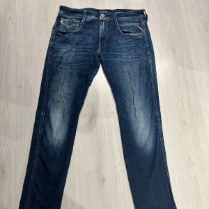 Blå Replay jeans straight fit - Snygga blå jeans från Replay modellen är anbass  med klassisk femficksdesign och raka ben. Jeansen har slitningar och kontrastsömmar, samt Replay-logga på bakfickan och vid myntfickan. Tillverkade i robust denim med en cool tvättad look. W31 / W32  finns en liten defekt på höger ben är ett super litet hål men inget som märks 