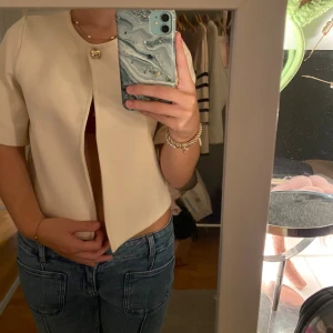 Beige kortärmad blus med knapp - Säljer en stilren beige blus med korta ärmar och en snygg guldig knapp framtill, från Gina Tricot💕💕