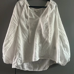 Vit linnemix blus från H&M - Luftig vit blus från H&M i linne med vida ärmar och v-ringning. Blusen har snörning vid halsen och är pösig och härlig. Det är storlek S men passar som M och kanske L också