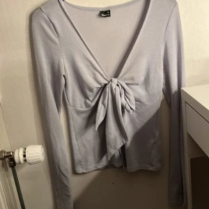 Ljusblå långärmad topp Gina Tricot XS - Supersnygg ljusblå långärmad topp från Gina Tricot i storlek XS. Toppen har djup v-ringning och en stor knyt-detalj framtill som ger en trendig look. Mjuk och stretchig i materialet, perfekt att styla med jeans eller kjol. Använd några gånger, den har även en lite fläck.
