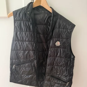 Moncler Gui väst - Svart Size 2. Som ni ser finns ett litet hål. Går enkelt att lösa men därför sänker jag priset på den. Köpt för 5-7 år sen nk i Göteborg så osäker på kvitto finns. Dock får ni gärna göra en lc om osäker