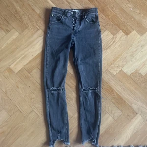 Svarta Gina Tricot Senna jeans med slitningar - Svarta jeans från Gina Tricot, modell Senna, med hög midja och knappar i gylfen. Jeansen har raka ben, slitna detaljer vid knäna och fransade benslut. Tillverkade i denim med en cool, lite tvättad look. Perfekta för dig som gillar en edgy stil.