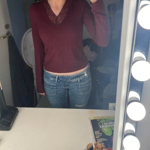 Vinröd långärmad topp med spets från Gina Tricot - Vinröd långärmad topp med v-ringning och dekorativ spets vid halsen. Snygg och enkel modell som sitter tajt mot kroppen. Perfekt för dig som gillar en stilren look med en liten twist.