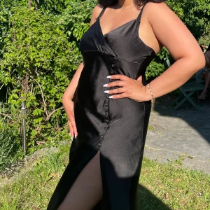 Svart midi satinklänning med knappdetalj på sidan - Endast använd en gång. storlek L. Köpt från Zara. Köparen står för frakten.