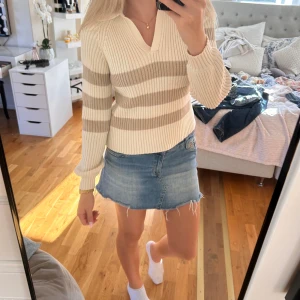 Randig ribbad tröja från NA-KD - Superfin ribbstickad tröja från NA-KD i beige och vit med breda ränder. Tröjan har krage, v-ringning och långa ärmar. Perfekt till jeans eller kjol för en chill och snygg look. Mjuk och skön kvalitet som känns lyxig.