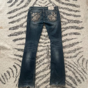 Miss Me bootcut jeans med broderi - Snygga blå bootcut jeans från Miss Me med slitningar och coola broderade bakfickor med paljettdetaljer. Jeansen har kontrastsömmar och klassisk femficksdesign. Materialet är bomull med lite stretch för skön passform. Jag köpte jeansen i London i oktober men dom är tyvärr lite stora och kommer inte till så mycket användning.