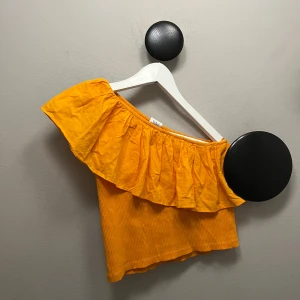 Orange offshoulder volangtop - Säljer en superfin orange offshoulder topp med bred volang runt hela överdelen. Toppen är croppad och har en ribbad struktur i tyget. Perfekt för dig som vill sticka ut med färg och volym i sommar!