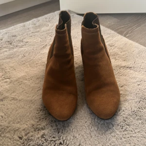 Bruna mockaboots med låg klack - Snygga bruna boots i mocka från DW med låg klack och rund tå. Skorna har en stilren design och passar perfekt till både jeans och kjol. De är i storlek 38 och har en klassisk siluett som funkar året runt.