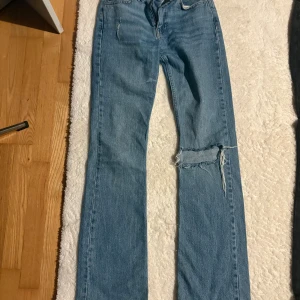 Blå bootcut jeans med slitning - Ett par ljusblå jeans med bootcut passform och snygg slitning över ena knät  med normal midja och raka ben. 