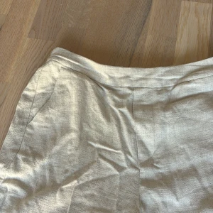 Beiga linnebyxor med rak passform - Snygga beiga linnebyxor med rak passform och diskreta fickor i sidorna. Byxorna har en enkel midja utan synliga detaljer och är tillverkade i ett lätt och luftigt linnematerial som passar perfekt för varmare dagar. Storlek S