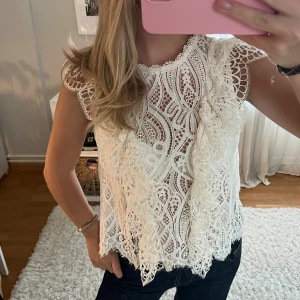 Vit spetsblus med volangdetaljer - Superfin vit blus i spets med vackert mönster och volangdetaljer framtill. Perfekt att styla med jeans eller kjol.