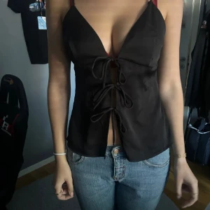 Svart satinlinnetopp med snörning - Säljer en svart linne-topp i satinliknande material med smala axelband och djup v-ringning. Toppen har snygg snörningsdetalj framtill. Säljer då den är förstår, aldrig använd helt ny! Är i storlek 38 men skulle säga att den e som en S.Tveka  inte på att höra av dig vid frågor!💕💕