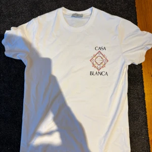 Vit Casablanca t-shirt med tryck - Vit t-shirt från Casablanca med färgglatt tryck och texten 'Casa Blanca' både fram och bak. Klassisk rund hals och korta ärmar. Materialet är mjuk bomull och designen har en sportig vibe med exklusiv känsla.