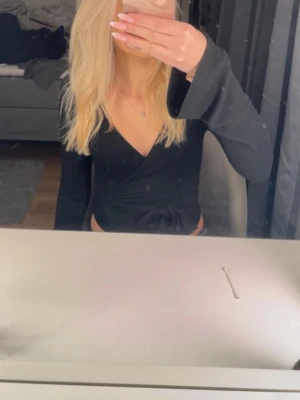 Svart omlottopp från Gina Tricot - Säljer en svart omlottopp från Gina Tricot i storlek XS. Toppen har långa ärmar, djup v-ringning och knyt i midjan. Materialet är mjukt och stretchigt, perfekt för att styla med både jeans och kjol. Enkel men ändå snygg detalj med omlott och knyt.