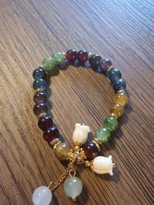 Pärlarmband med berlocker - Ett vackert pärlarmband med olika färgade pärlor och berlocker i form av blommor och runda hängen. Armbandet har guldfärgade detaljer.