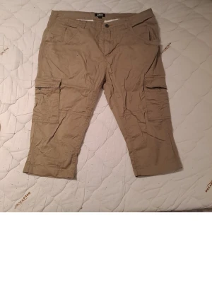 Beiga cargopants från William Baxter - Säljer ett par beiga cargopants från William Baxter i storlek L. Byxorna har flera praktiska fickor på sidorna och baktill, samt ett trekvarts-snitt som ger en avslappnad look. Tillverkade i bomull för skön känsla och andningsförmåga.