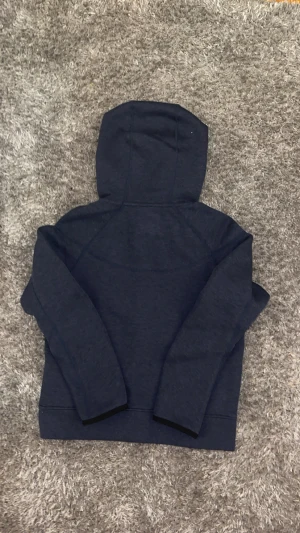 Mörkblå Nike hoodie med dragkedja - Snygg mörkblå hoodie från Nike med hel dragkedja och huva. Tröjan har svarta detaljer vid fickorna och Nike-logga på bröstet. Tillverkad i mjuk bomullsmix, perfekt för chill eller träning. Långärmad och med bekväm passform. Pris kan diskuteras 