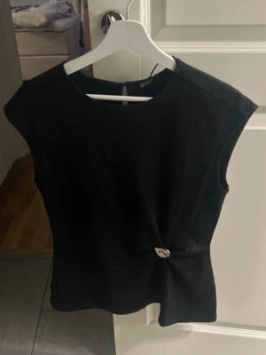 Svart topp Stockh lm - Svart topp från Stockh lm, den har en snygg twist framtill med en silverfärgad metallknapp som detalj. Aldrig använd! Storlek M men passar S💗💗🌸