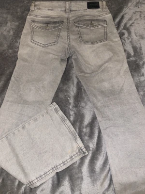 Grå bootcut jeans från Gina Tricot - Säljer ett par ljusgrå jeans från Gina Tricot, modell 'perfect jeans'. De har bootcut passform och klassiska fickor med lock och knapp bak. Jeansen är i mjukt denimtyg och har bälteshällor i midjan. Perfekta för dig som gillar en retro vibe.