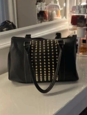 Svart handväska  - Säljer en svart handväska med guldiga nitar på framsidan pris kan diskuteras original priset var 500 