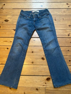 Levi's Marissa Bootcut Jeans Blå - Säljer ett par klassiska Levi's Marissa bootcut jeans i blå tvätt. Jeansen har låg midja, fem fickor och snygga kontrastsömmar. Materialet är slitstarkt jeans och passformen är relaxed med utsvängda ben. Perfekta för dig som gillar retrovibbar och tidlös stil. Priset kan diskuteras. Skriv vid frågor om mått eller något annat😊
