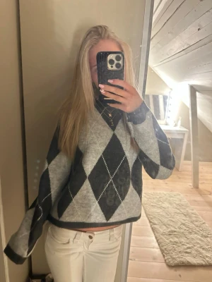 Grå rutig stickad tröja - Säljer en stickad tröja med klassiskt argylemönster i grått. Tröjan har lång ärm, hög hals och en loose passform. Perfekt för dig som gillar en chill och stilren look. Så snygg!🥰