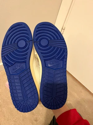 Nike Air Jordan 1 Low Travis Scott blå/vit - Nike Air Jordan 1 Low Travis Scott i vitt och blått skinn med ikonisk omvänd Swoosh, blå yttersula och broderade detaljer på hälen. Skorna har snörning, perforerad tå och klassisk Air Jordan-logga. Perfekta för dig som vill sticka ut med en hypad sneaker.